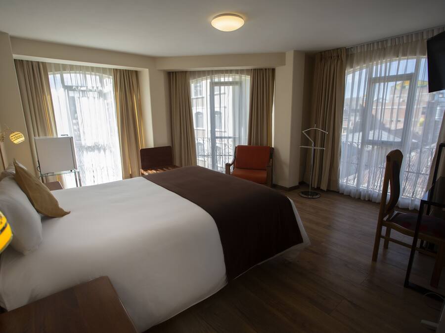 A hotel room with a large bed, a desk, a chair, and a TV.