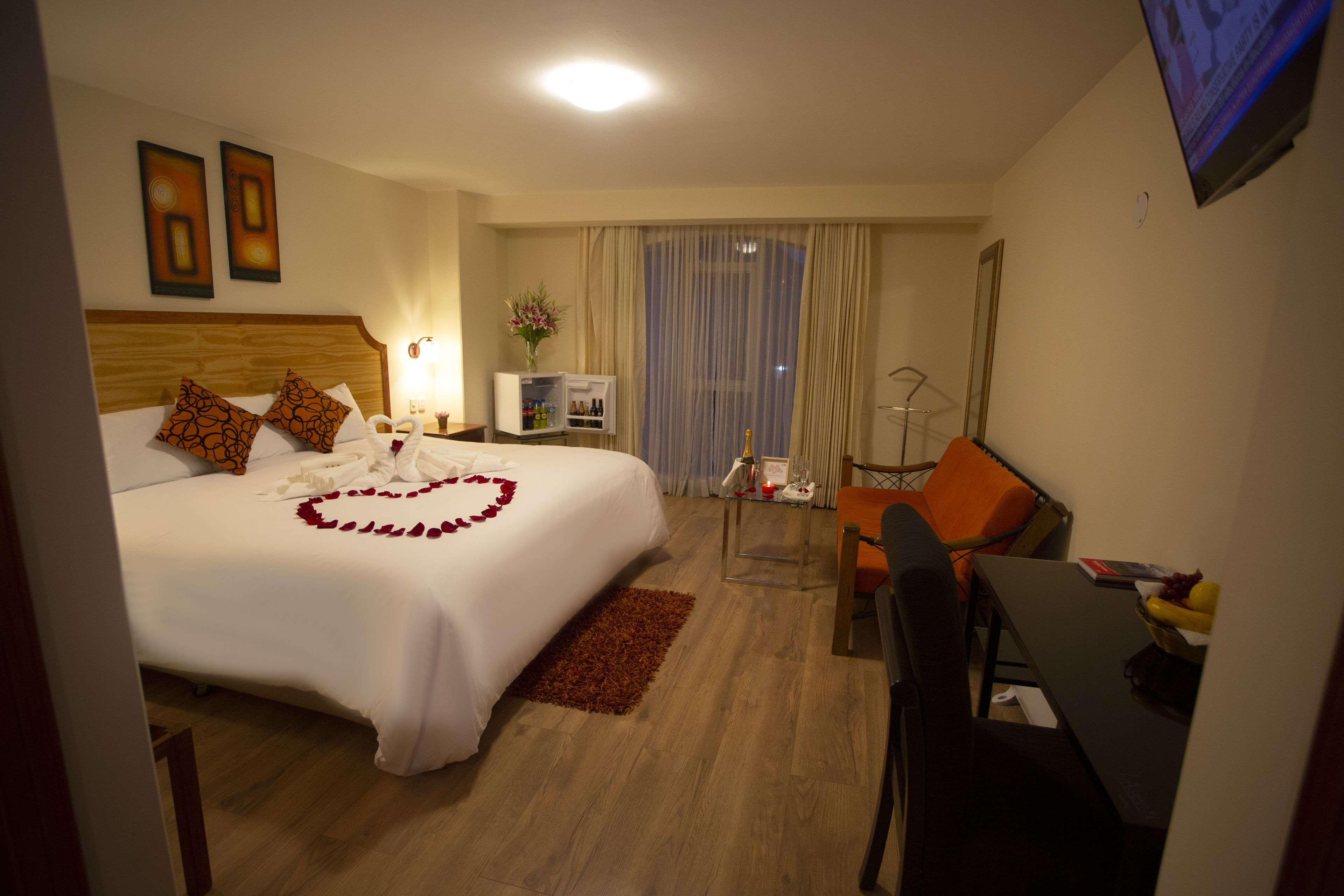 A hotel room with a bed, a desk, a chair, a TV, and a window with curtains.