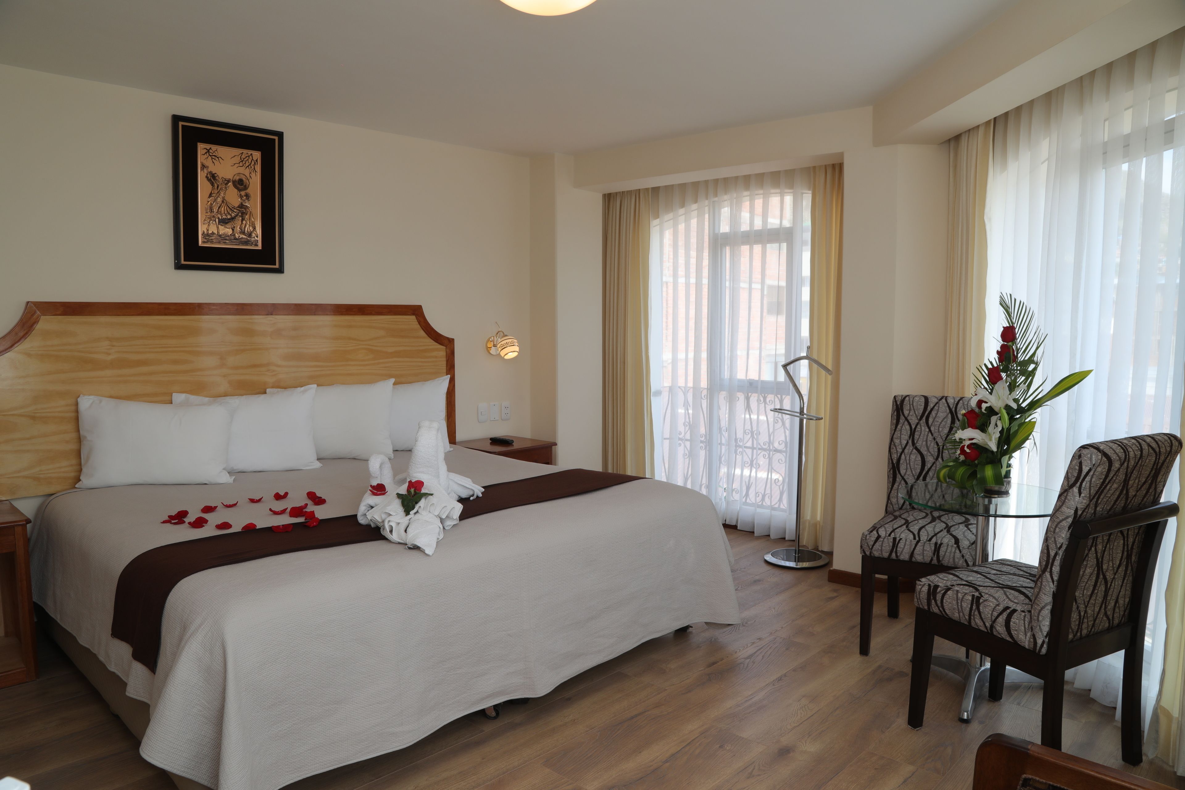 A hotel room with a large bed, a chair, a table with a vase, and a picture on the wall.