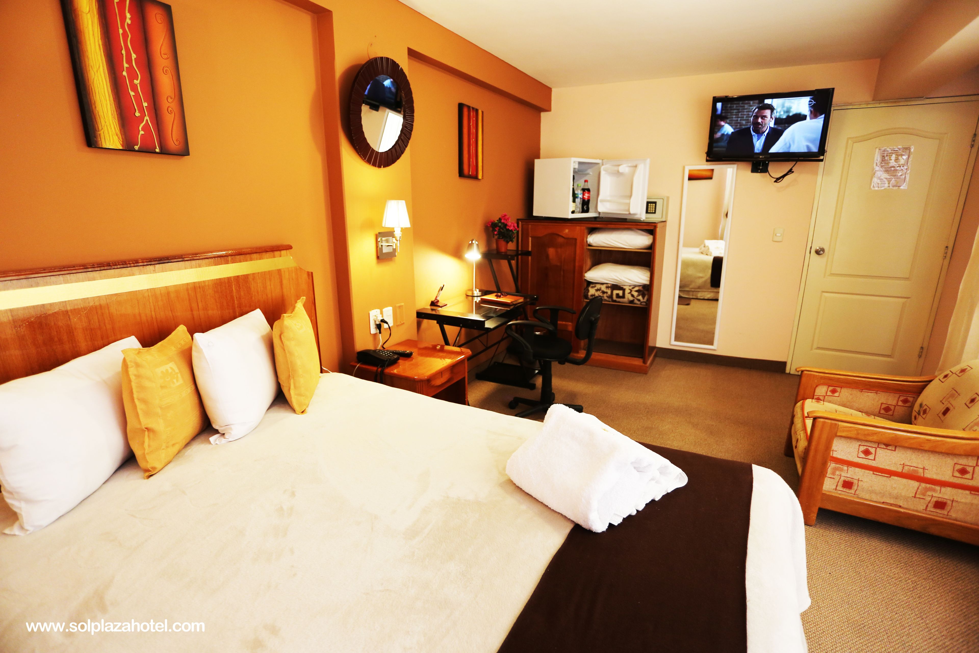 A hotel room with a large bed, a desk, a chair, a television, and a wardrobe.