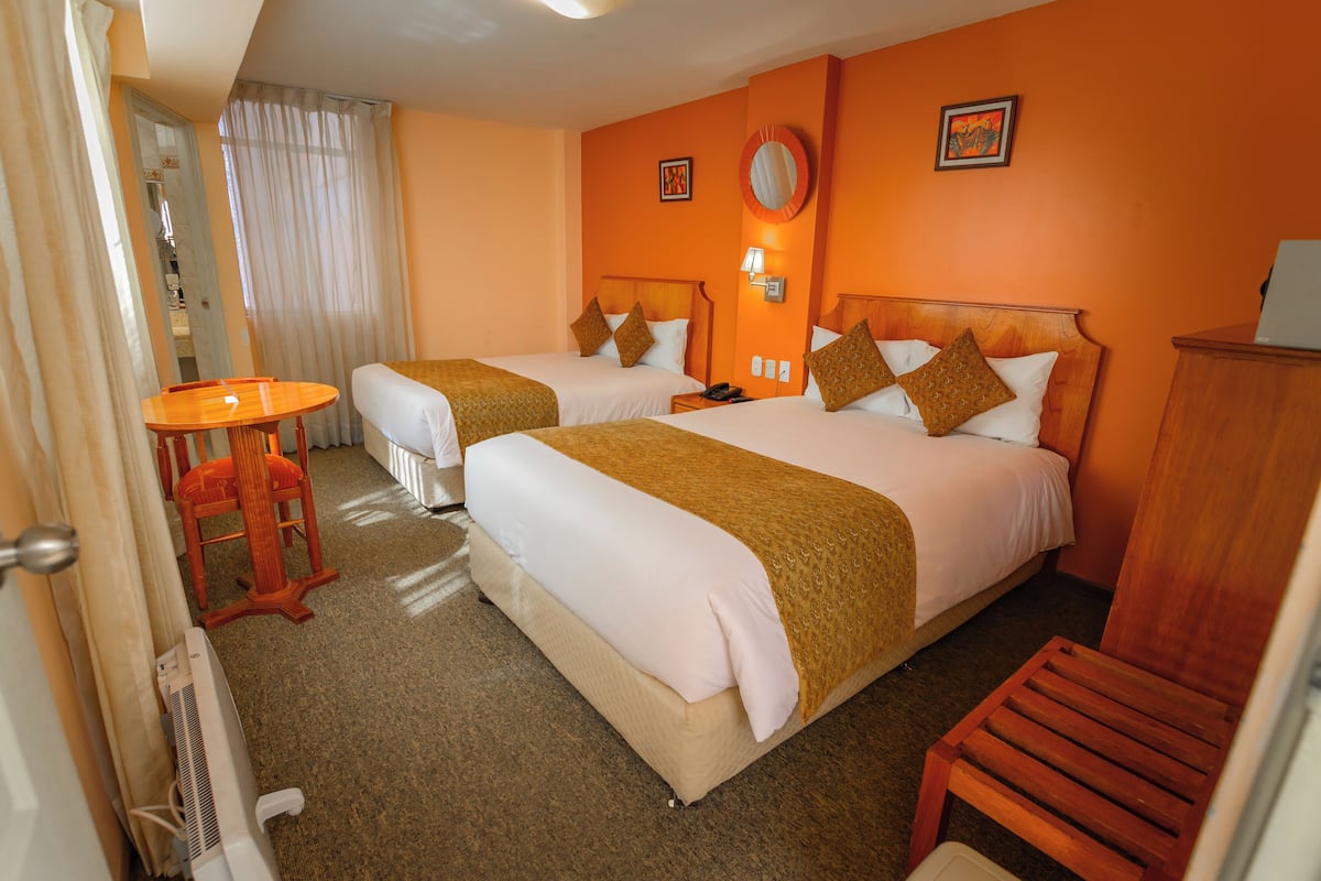 Habitación de hotel con dos camas, una silla de madera, una mesita y un calentador.