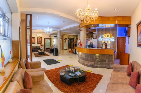 A hotel lobby with a reception desk, seating area, chandelier, and artwork.