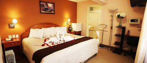 A hotel room with a large bed, two bedside lamps, a flat-screen TV, a desk with a chair, and a painting on the wall.