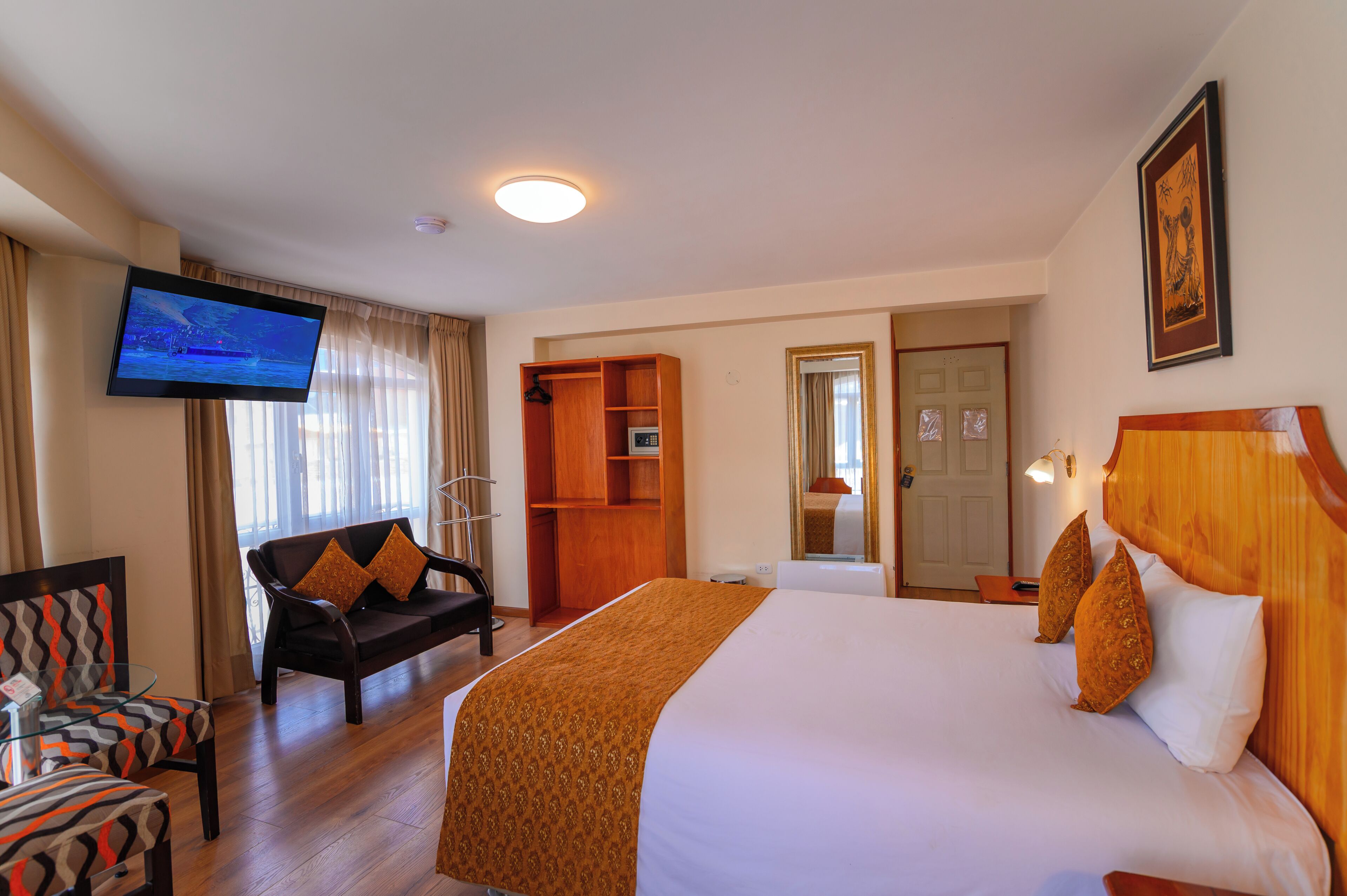A hotel room with a bed, a TV, a seating area, and a wardrobe.