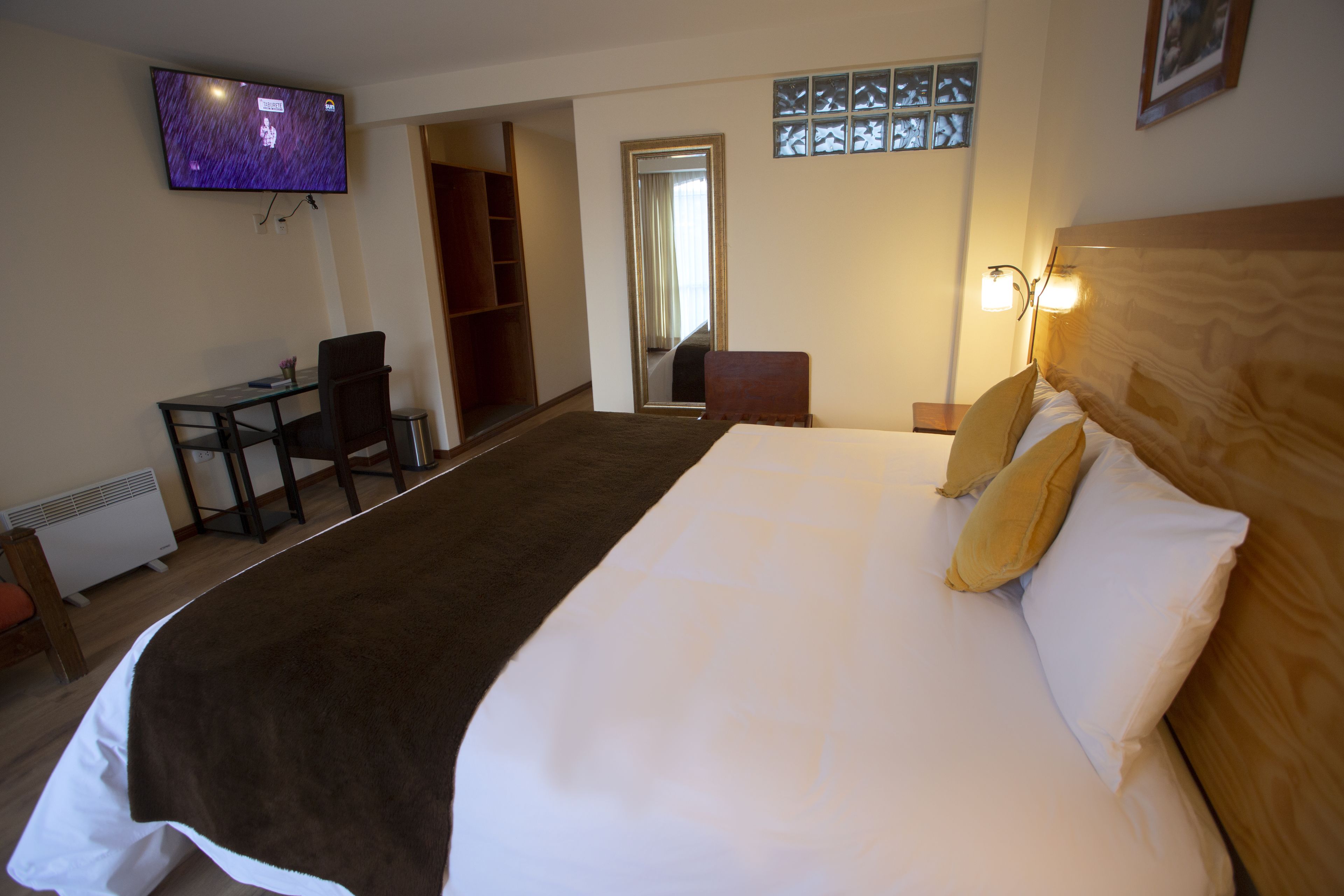 A hotel room with a large bed, a desk, a chair, a TV, and a wardrobe.