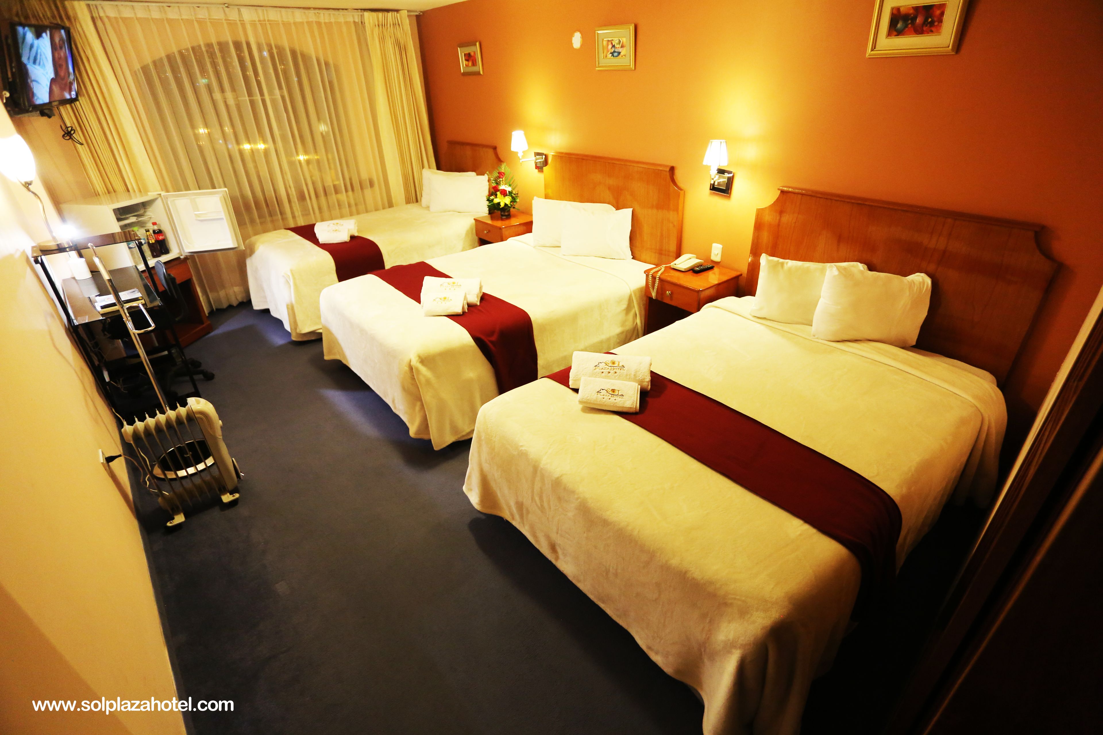 Ein Hotelzimmer mit drei Betten, einem Fernseher und einer Minibar.