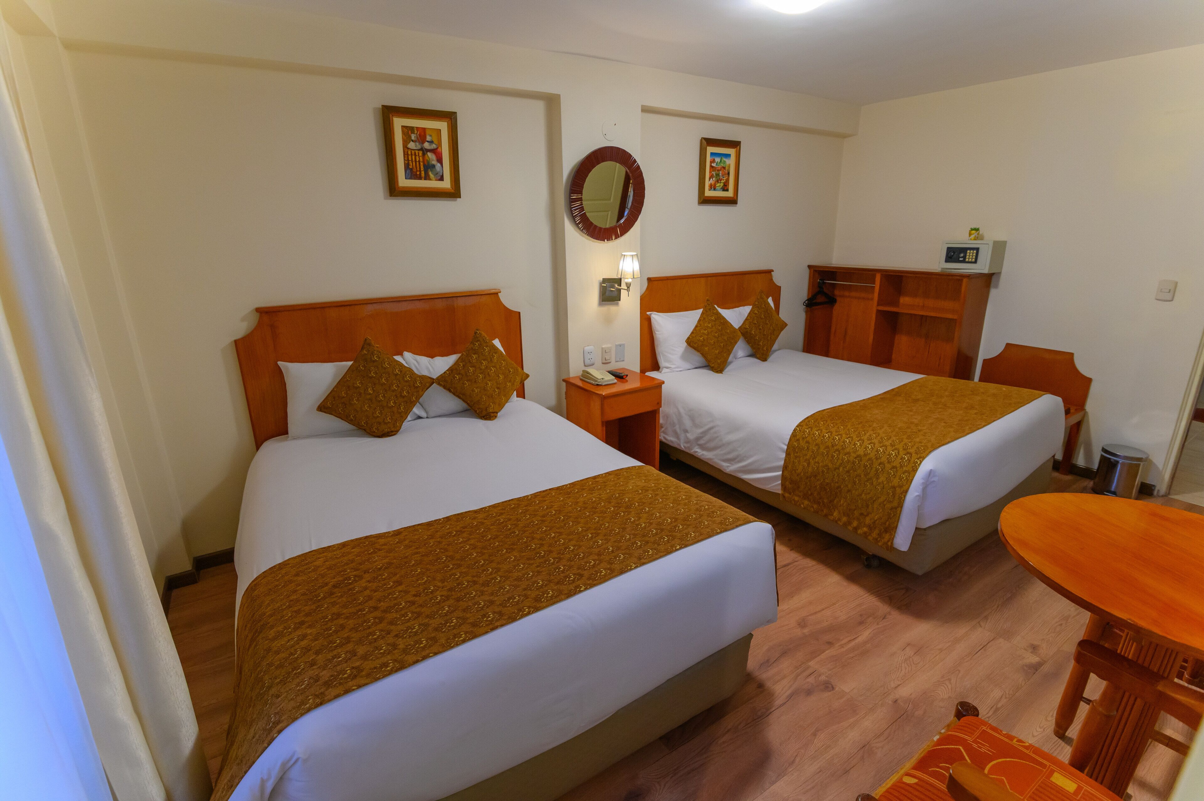 Two double beds with wooden headboards, a small table, and a wall-mounted mirror.
