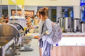 Zona de bufé con diversas opciones de comida y una persona servándose.