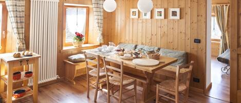 A wooden interior with a dining table, chairs, a sofa, and a window with curtains.