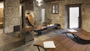 A stone-walled room with a fireplace, a bench, and two lounge chairs. - Albergo Diffuso Sauris In Sauris di Sopra (Sauris)