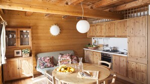 A wooden interior with a dining table, chairs, a kitchen area, and a sofa with floral cushions. - Albergo Diffuso Sauris In Sauris di Sopra (Sauris)
