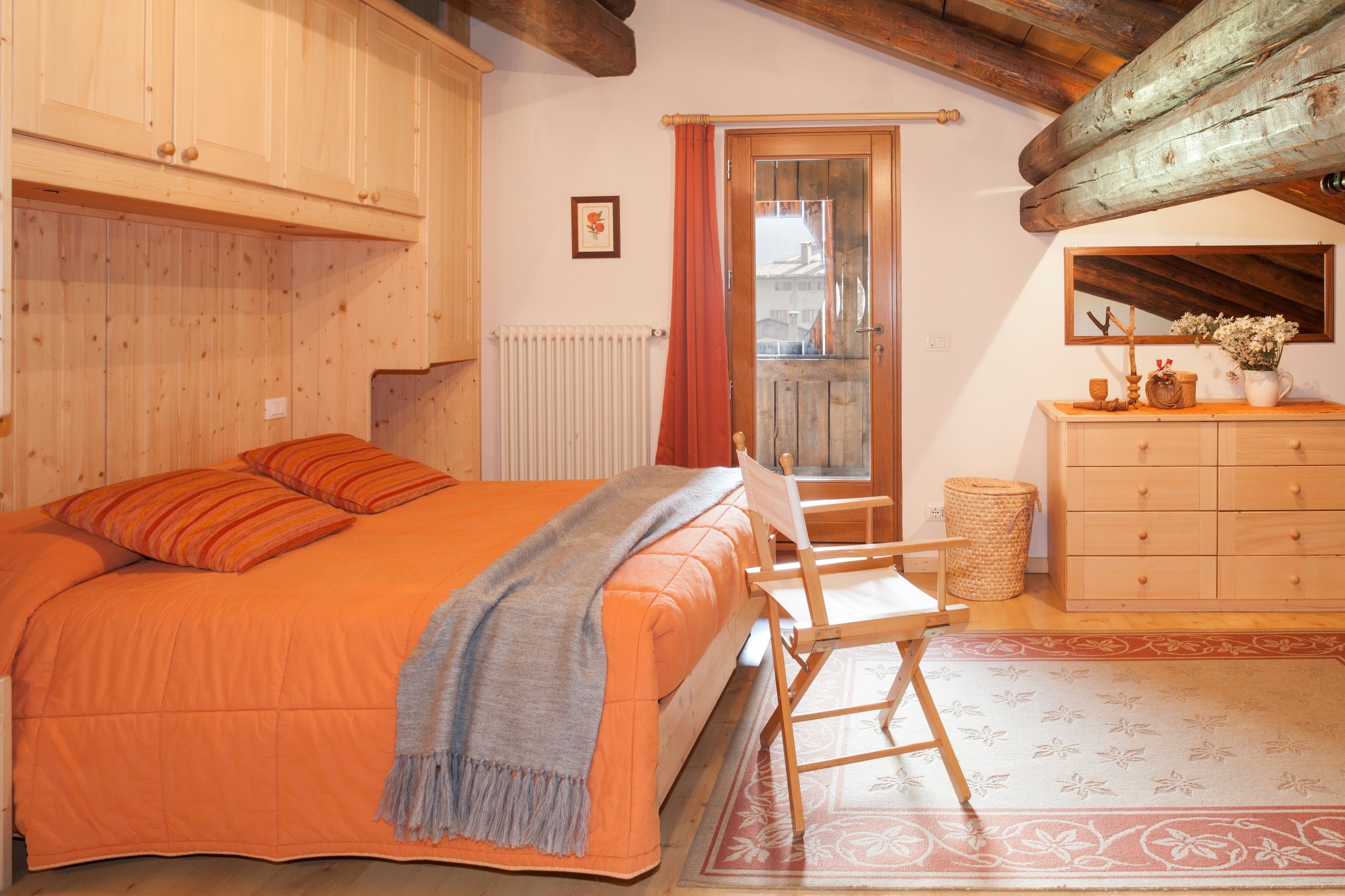 Une chambre à coucher avec un lit, une commode, une chaise, une fenêtre et un plafond en bois.
