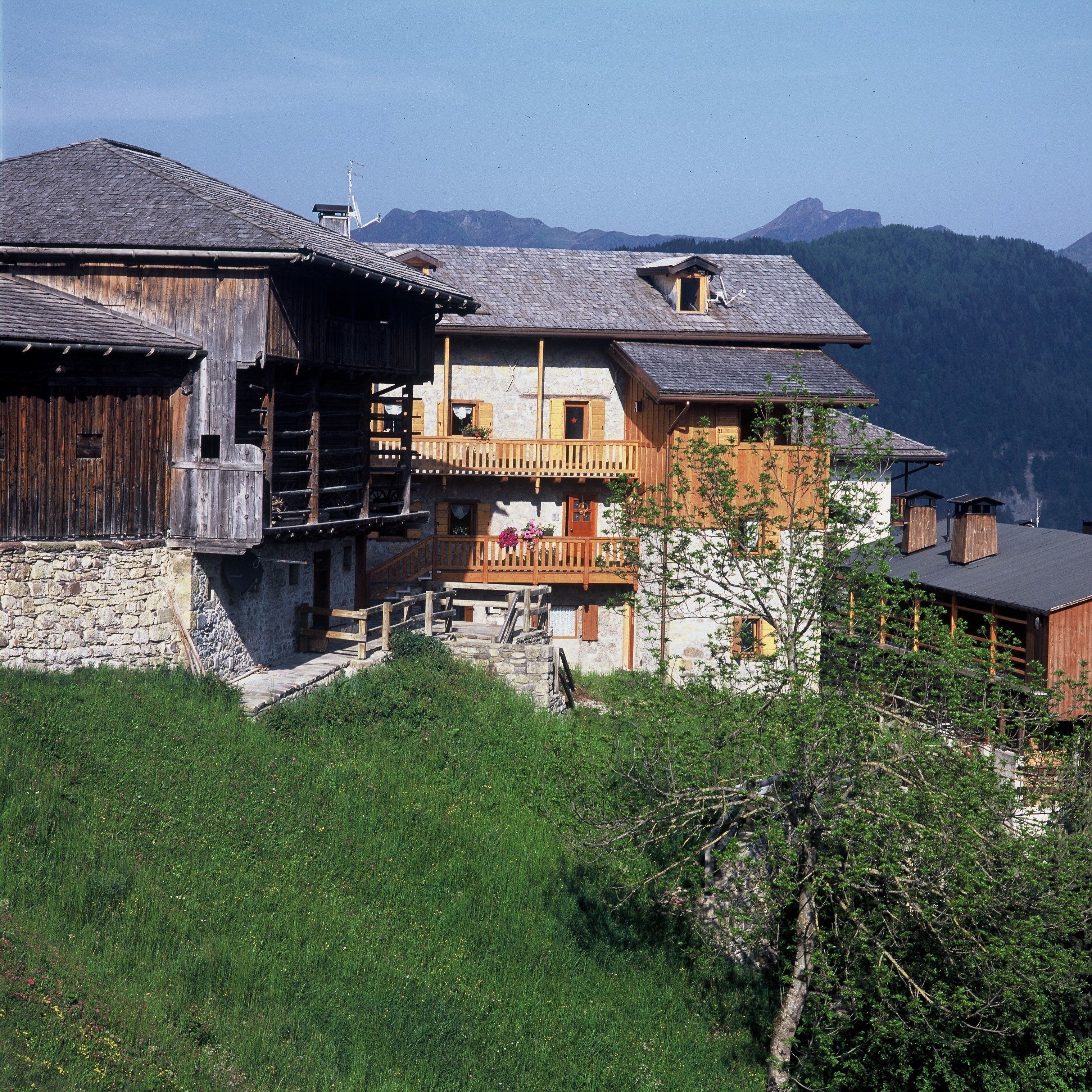 Een traditioneel chalet met een stenen fundering, houten balkons en een uitzicht op bergen op de achtergrond.