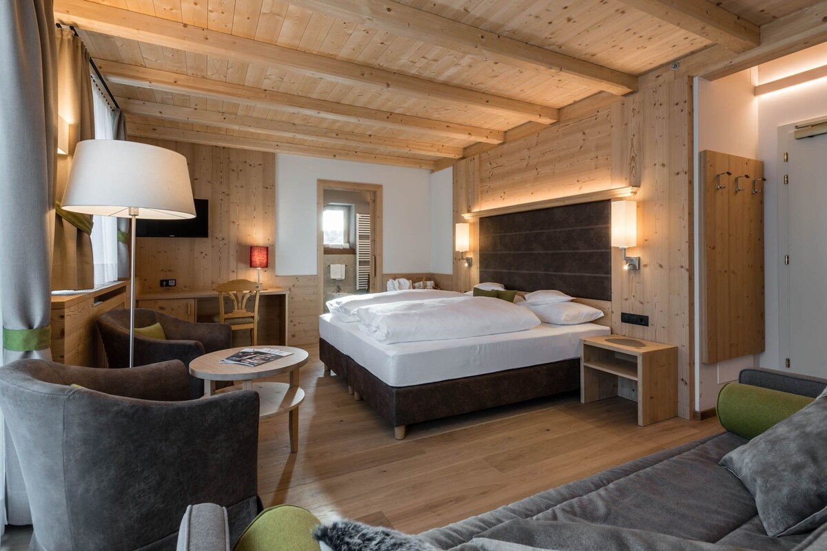 A hotel room with a large bed, a desk, a chair, and a sofa.