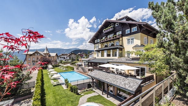 A hotel with a swimming pool, outdoor seating, and a view of mountains. - Hotel Villa Kastelruth (Castelrotto)