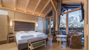 A wooden room with a bed, a table, and a chair. There is a window with a view of mountains. - Hotel Villa Kastelruth (Castelrotto)