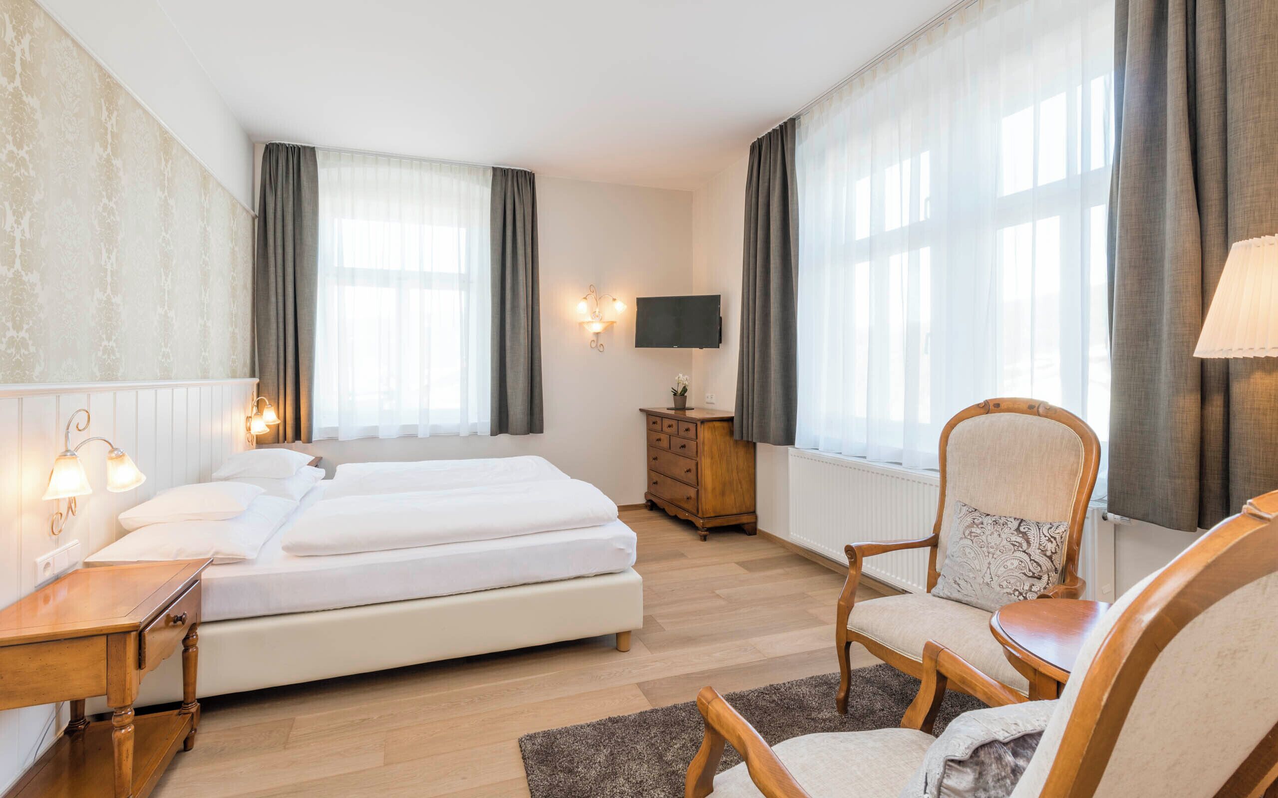 Quarto de hotel com duas camas, uma cômoda de madeira, uma cadeira, uma televisão e um abajur.