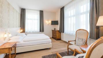Quarto de hotel com duas camas, uma cômoda de madeira, uma cadeira, uma televisão e um abajur.