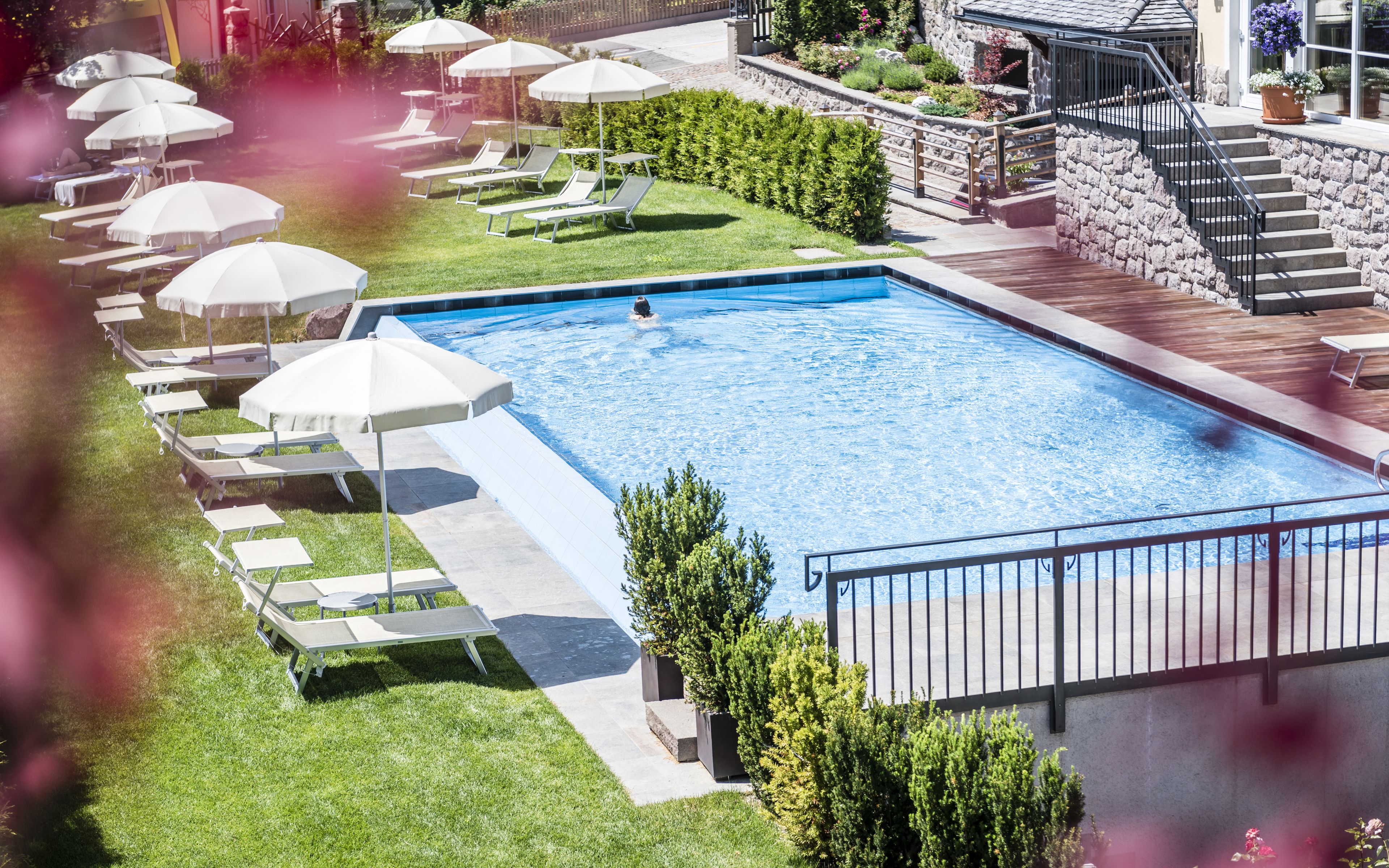 Una piscina con sillas de descanso y sombrillas, rodeada por un muro de piedra y una terraza de madera.