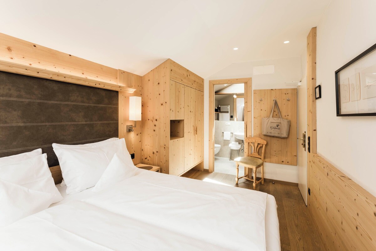 A hotel room with a wooden headboard, a bed with white linens, a wooden wardrobe, and a small wooden bench.