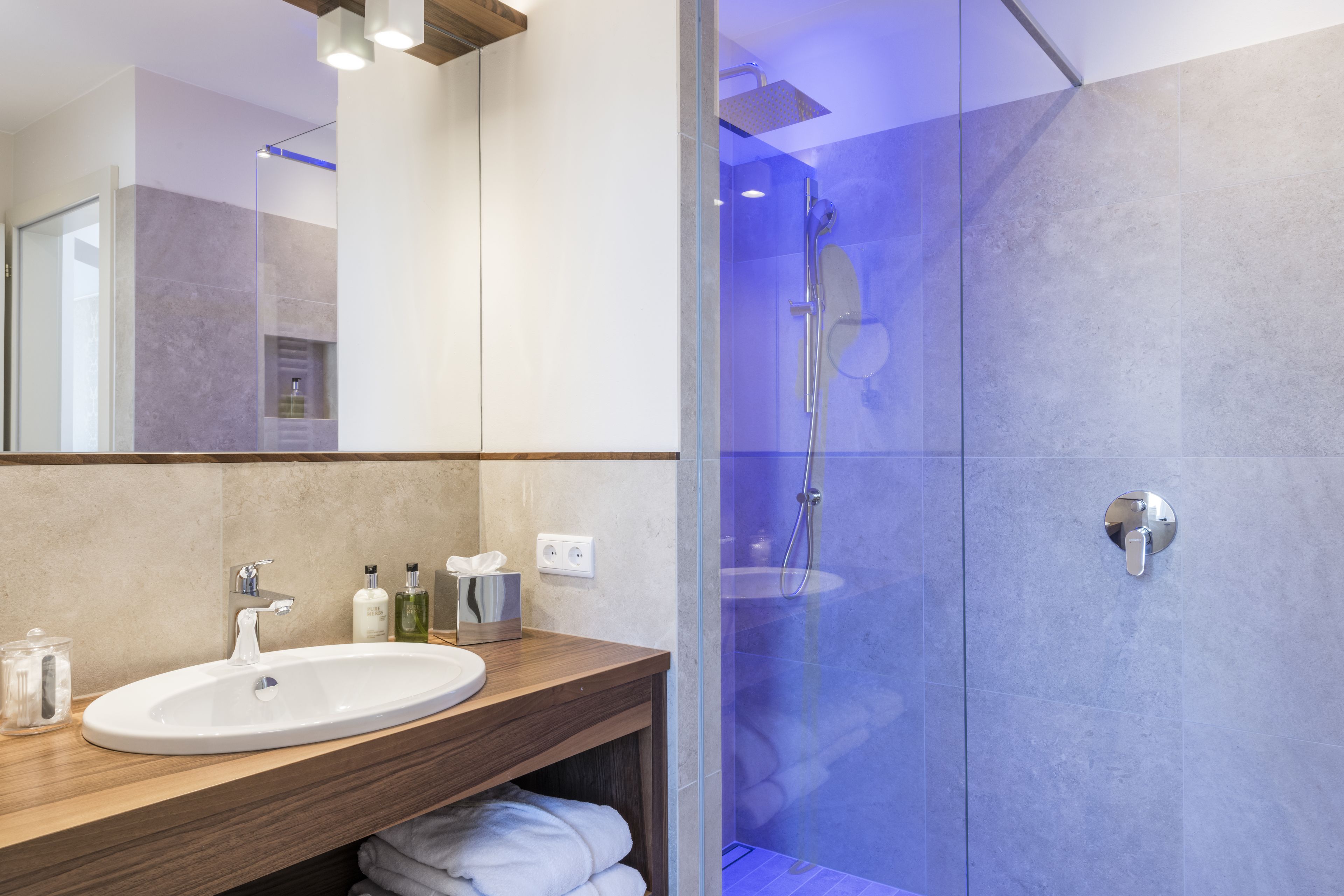 A modern bathroom with a wooden vanity, a white sink, and a glass-enclosed shower area.