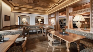 A restaurant with wooden furniture, patterned cushions, and a bar area with shelves of bottles. - Hotel Villa Kastelruth (Castelrotto)