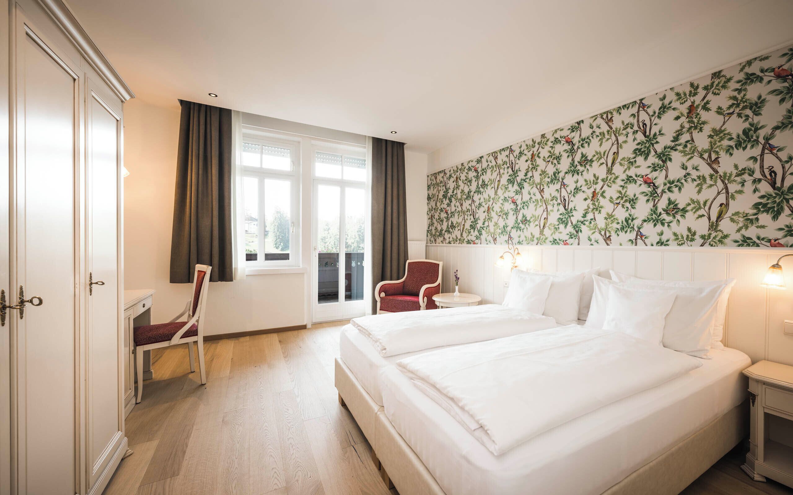 Habitación de hotel con dos camas, una silla, una mesita y una ventana con cortinas.