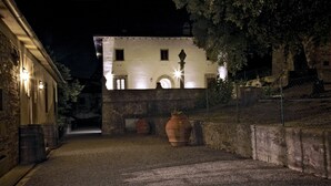 A nighttime view of a historic building with a stone facade, illuminated windows, and a paved courtyard. - Agriturismo Colognole (Pontassieve)