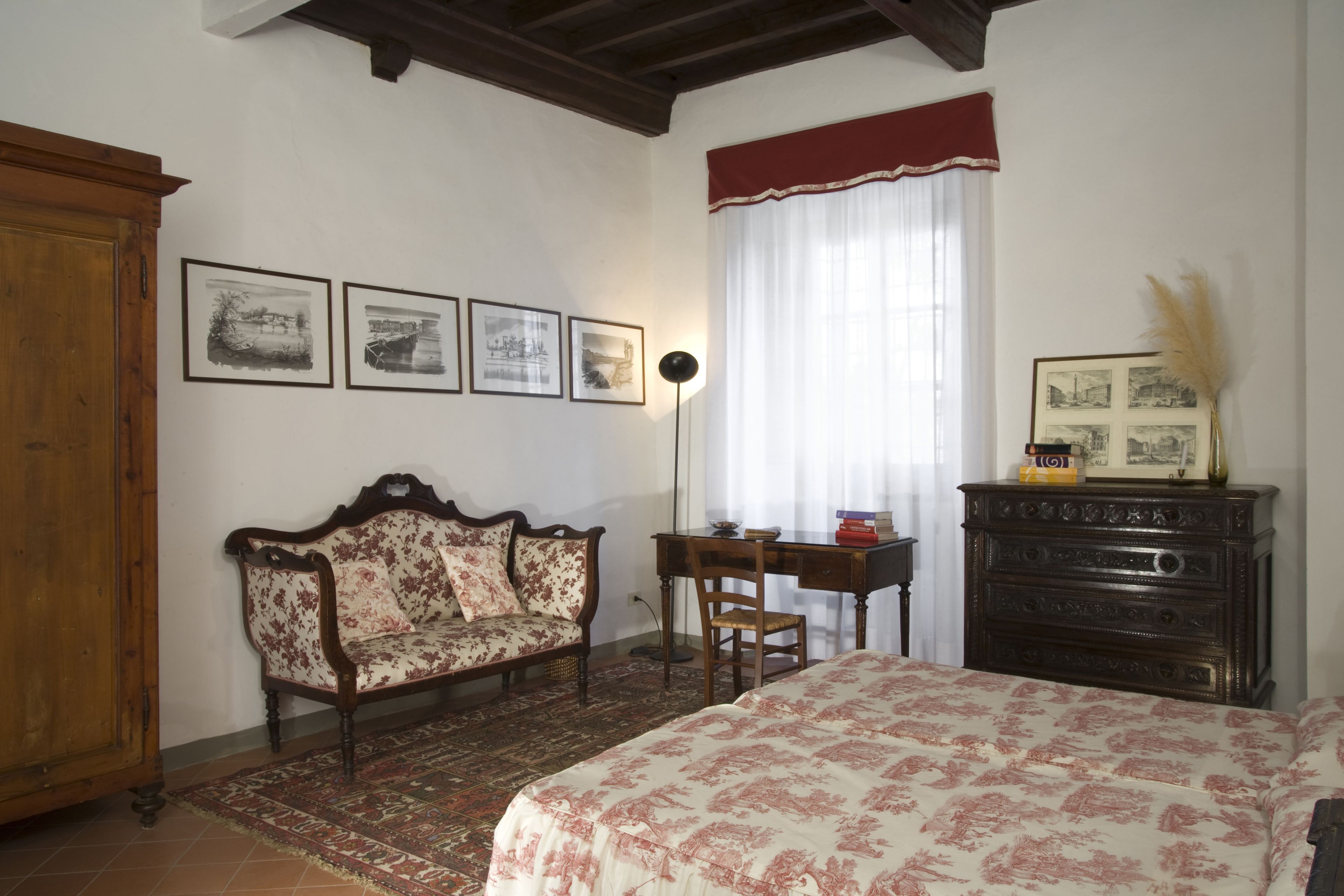 A bedroom with a bed, a wooden dresser, a desk, a chair, a sofa, and a window with curtains.