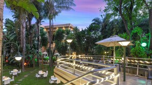 A well-lit outdoor area with a staircase, seating, and tables, surrounded by lush greenery and palm trees. - Villa Simonne (Johannesburg)