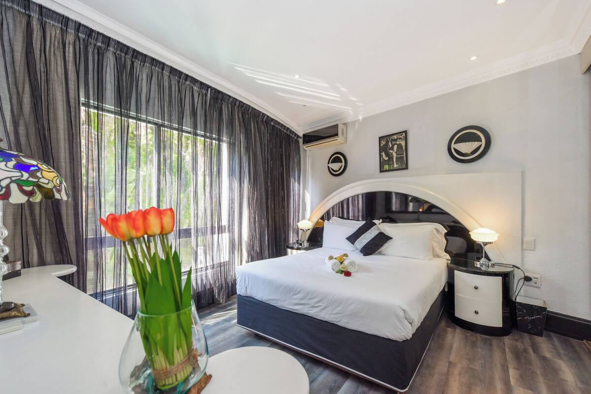 Una habitación de hotel con una cama grande, una mesita de noche, un escritorio y una ventana con cortinas.