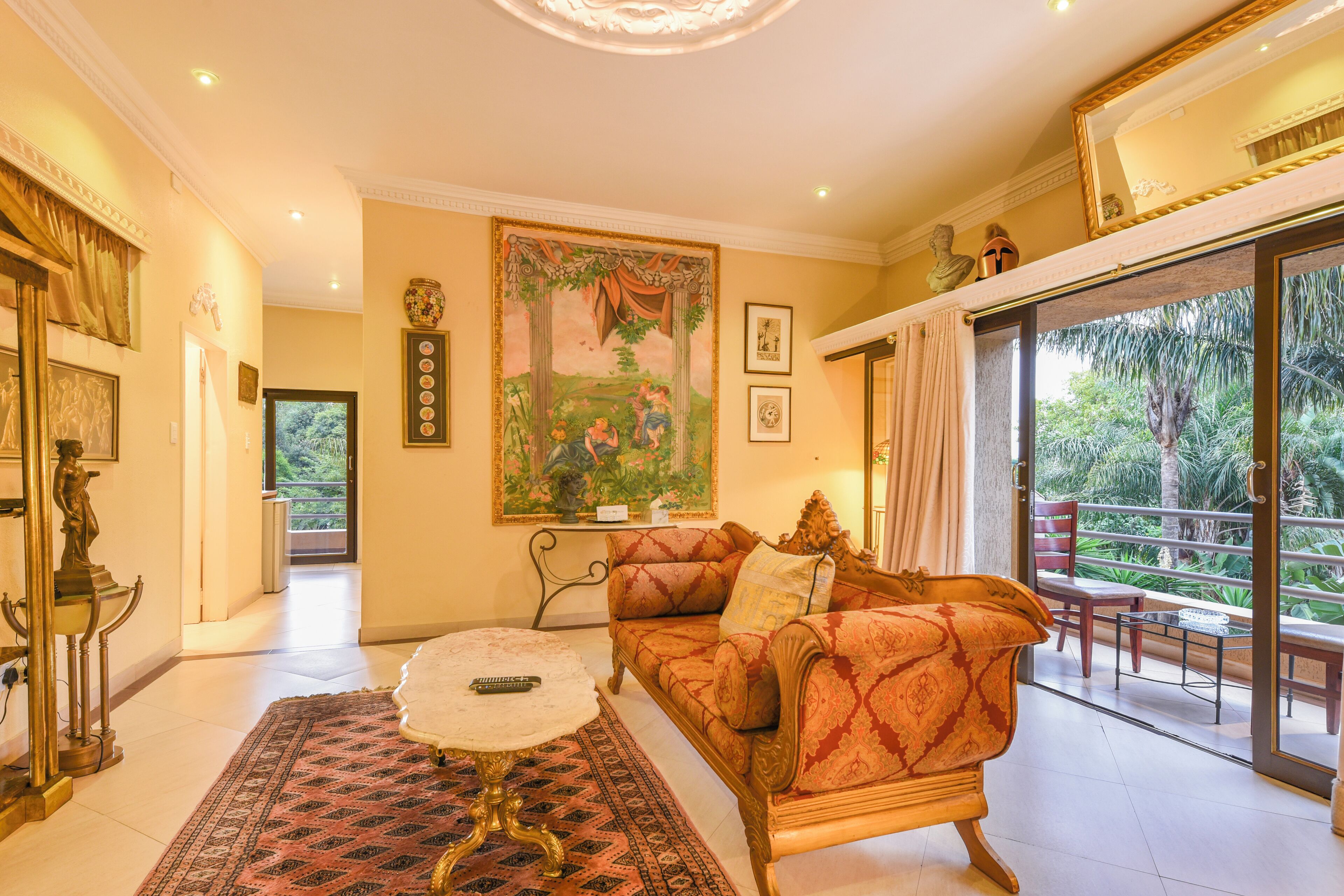 A spacious living room with a large sofa, a coffee table, and a view of a balcony with outdoor furniture.