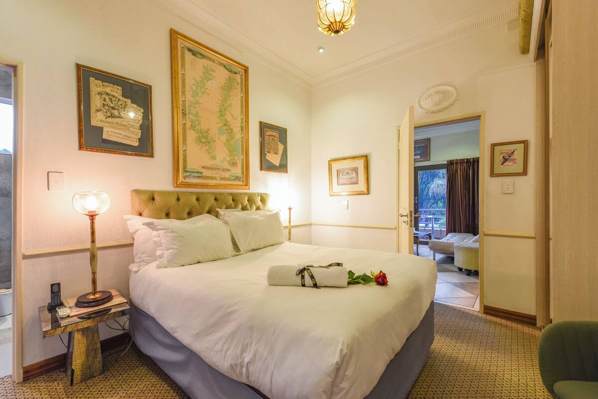 Una habitación de hotel con una cama grande, una mesita de noche con lámpara, un mapa enmarcado en la pared y una puerta que da a un balcón.