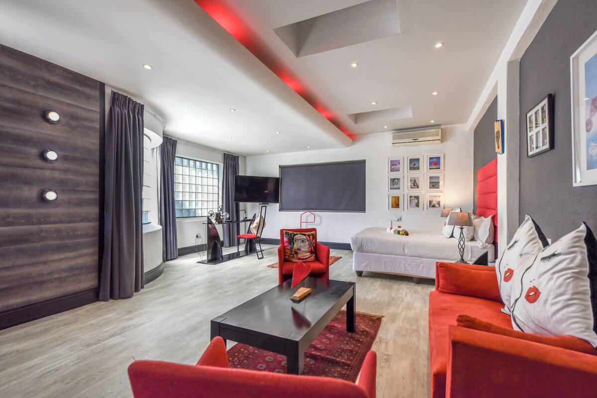Una sala moderna con un televisor de pantalla plana grande, un sofá rojo, una cama blanca y una pared de acento roja.