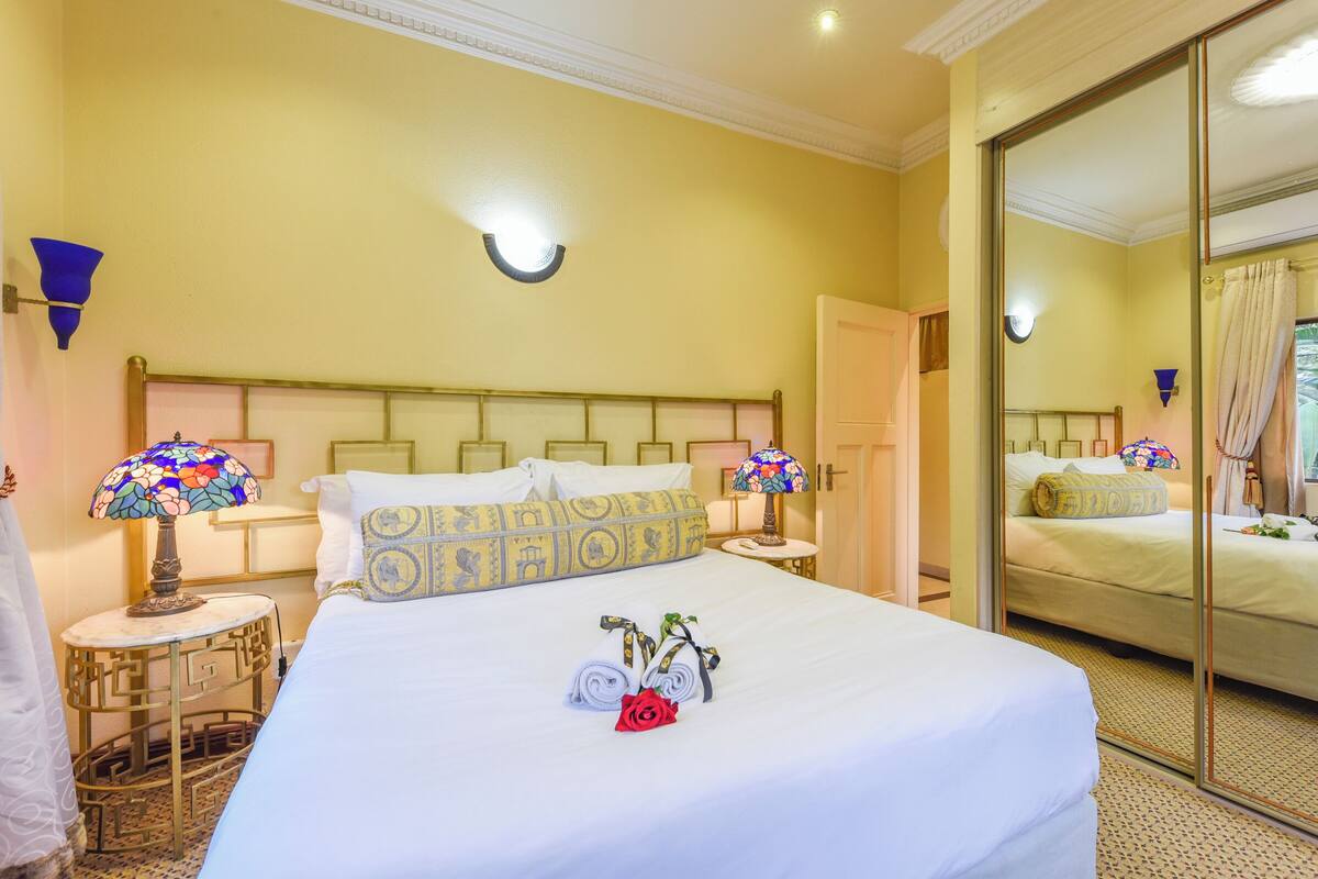 Habitación de hotel con una cama grande, dos lámparas de noche, un espejo y una mesita con lámpara.