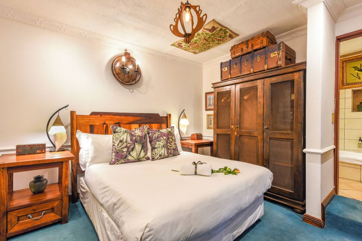 Habitación de hotel impecable con una cama grande, cabecera de madera, armario, mesita de noche con lámpara y una lámpara decorativa en el techo.