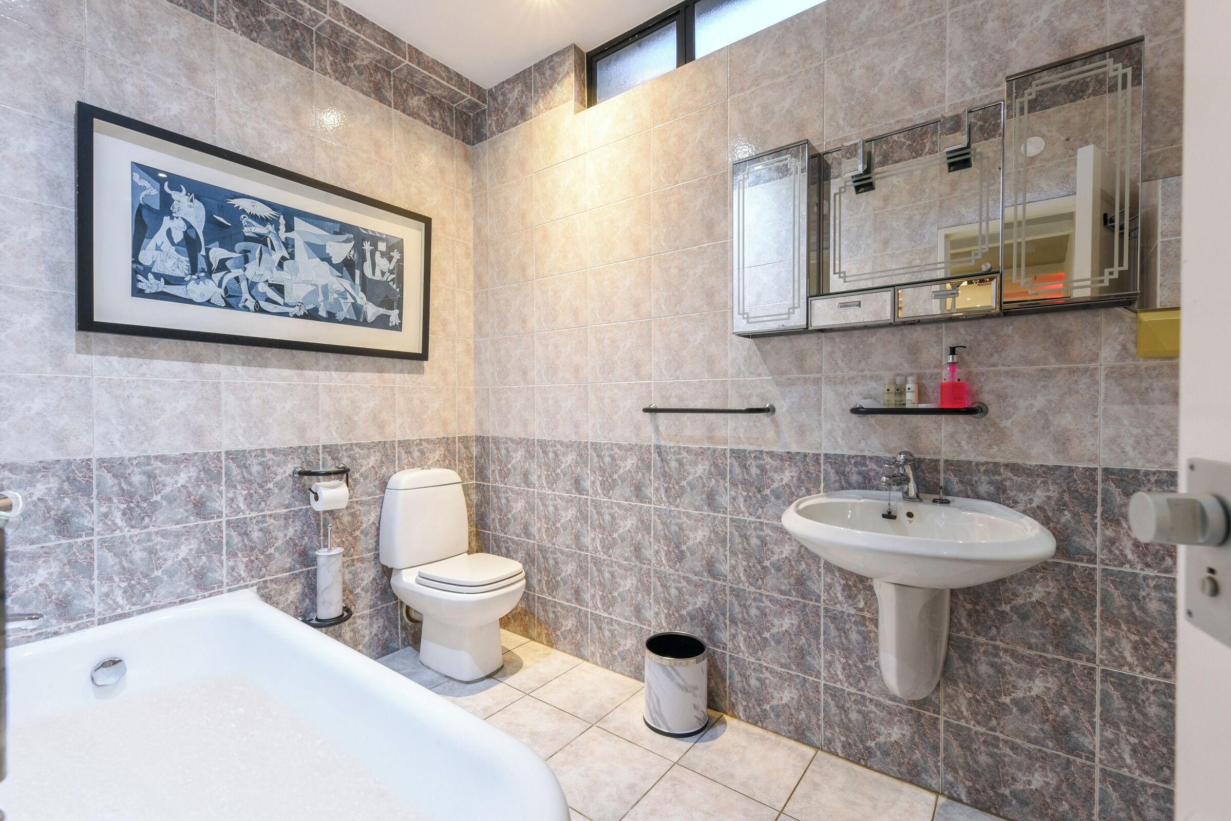 A modern bathroom with a bathtub, toilet, sink, and a framed artwork on the wall.