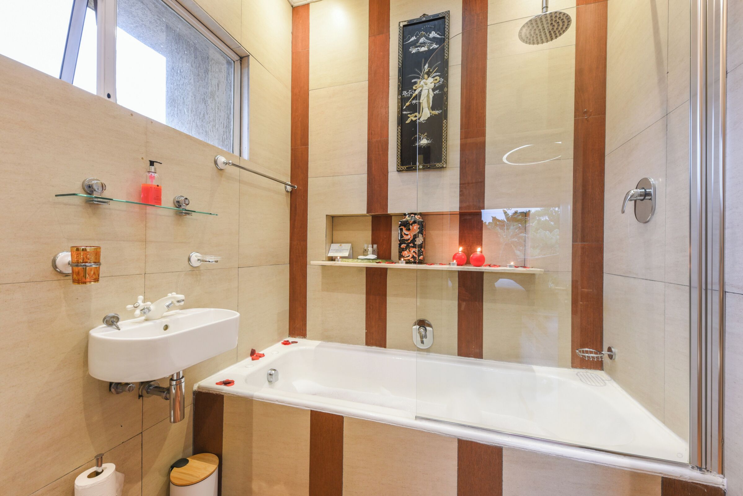 A modern bathroom with a bathtub, two sinks, a glass shower enclosure, and decorative items on shelves.