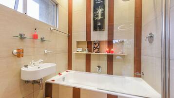 A modern bathroom with a bathtub, two sinks, a glass shower enclosure, and decorative items on shelves.