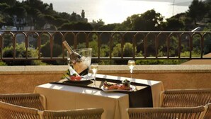 Mesa posta para dois, com uma garrafa de champanhe, uma taça de vinho e um prato de comida, com vista panorâmica para um corpo d'água e colinas.
