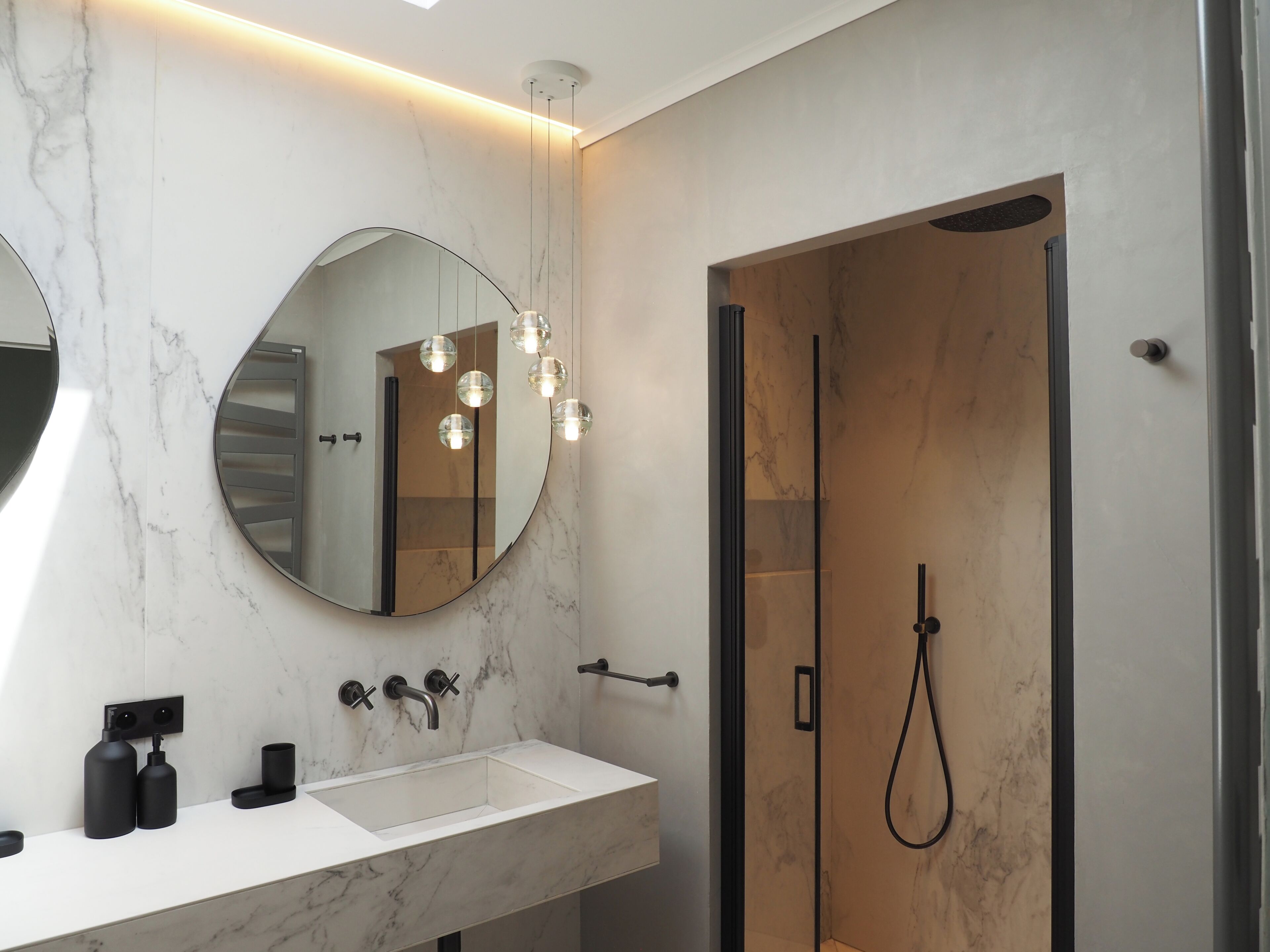 Un baño moderno con tocador de mármol, un espejo grande, cabina de ducha de vidrio e iluminación colgante.