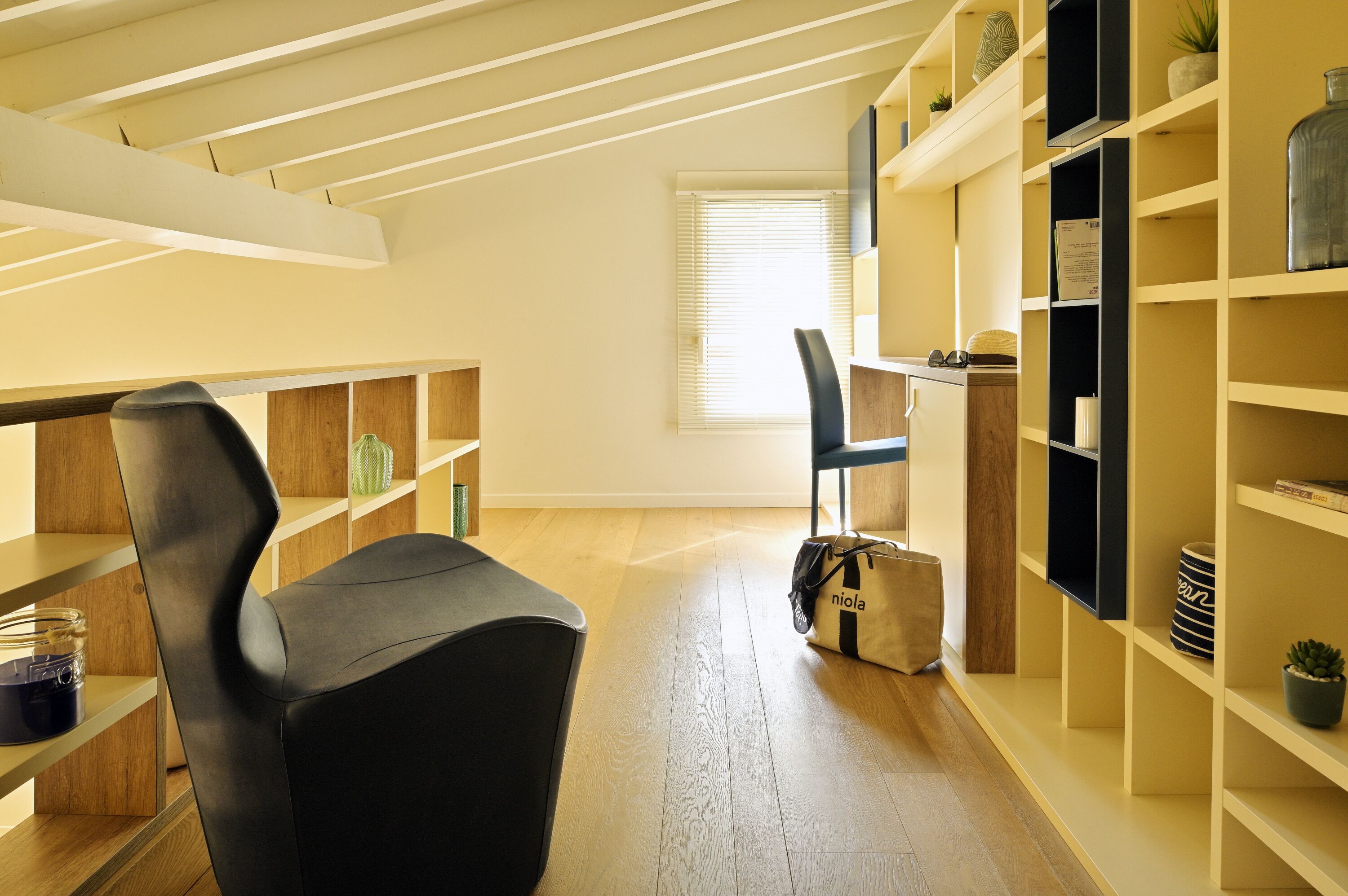 A modern room with a black chair, wooden shelves, and a window with blinds.