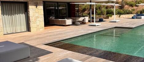 A modern house with a swimming pool, outdoor seating, and a view of the surrounding landscape.