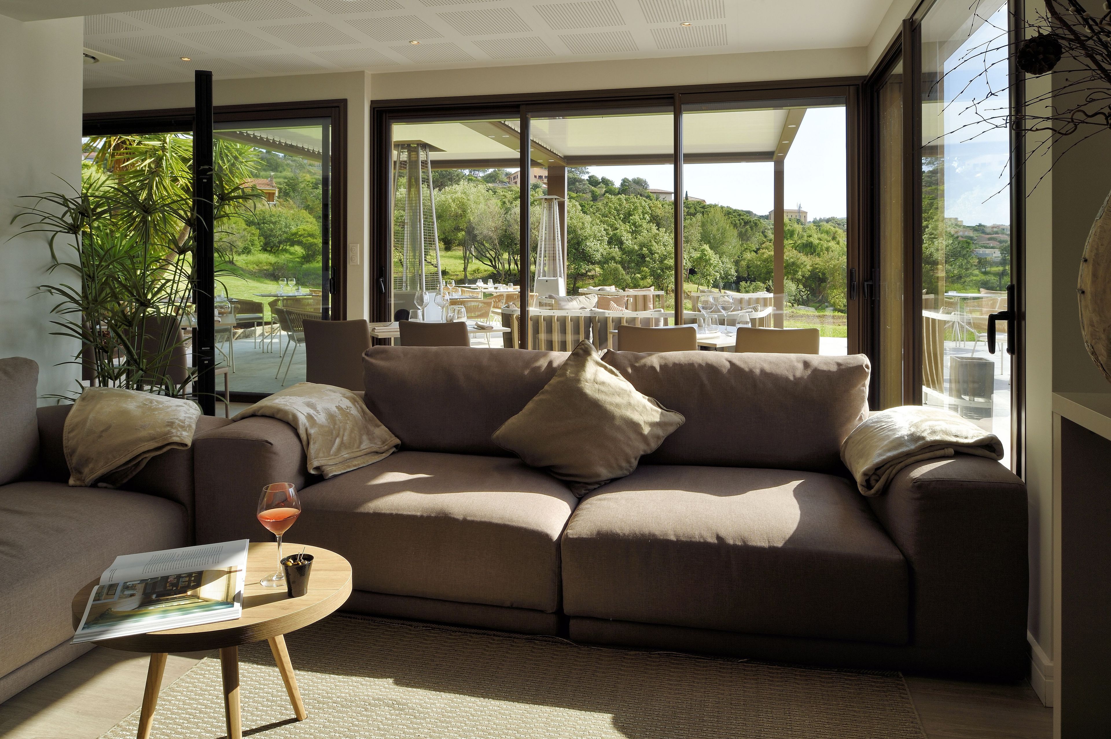 A modern living room with a large window, a sofa, a coffee table, and a glass of wine.