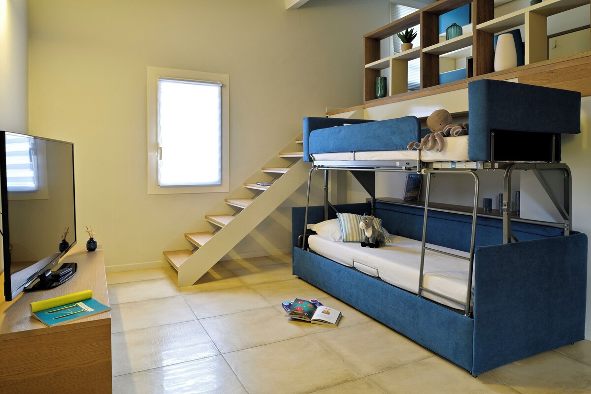 A compact room with a bunk bed, a TV, a desk, and a staircase.