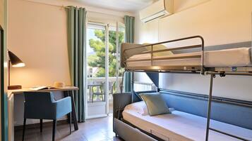 Una litera con escritorio y silla, una ventana con cortinas, y un equipo de aire acondicionado.