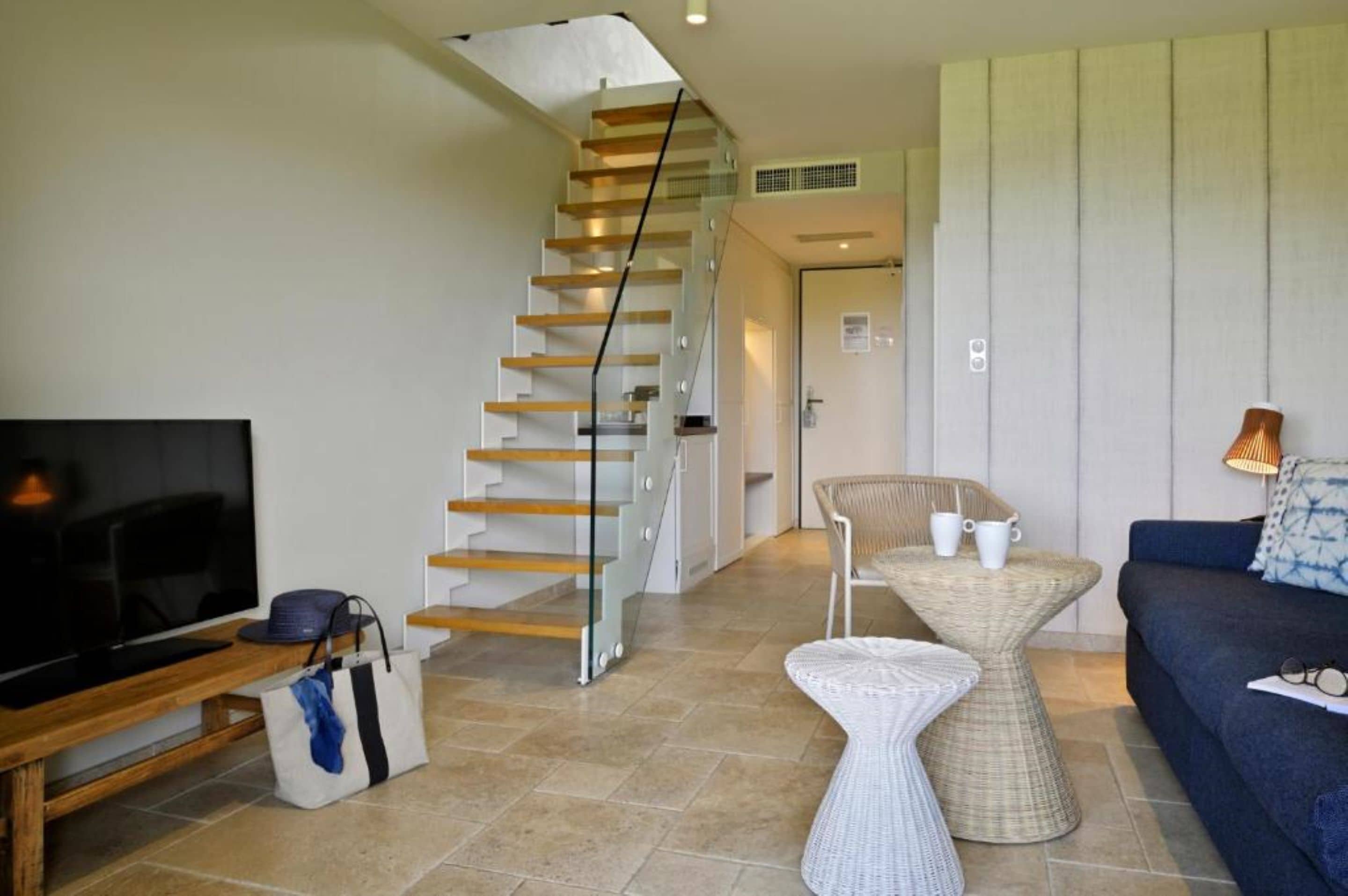 Uma sala de estar moderna com escada de madeira, televisão de tela plana, sofá e mesa lateral de vime.