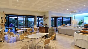 Uma sala de jantar ampla com mesas e cadeiras, um buffet e grandes janelas com vista para o exterior.