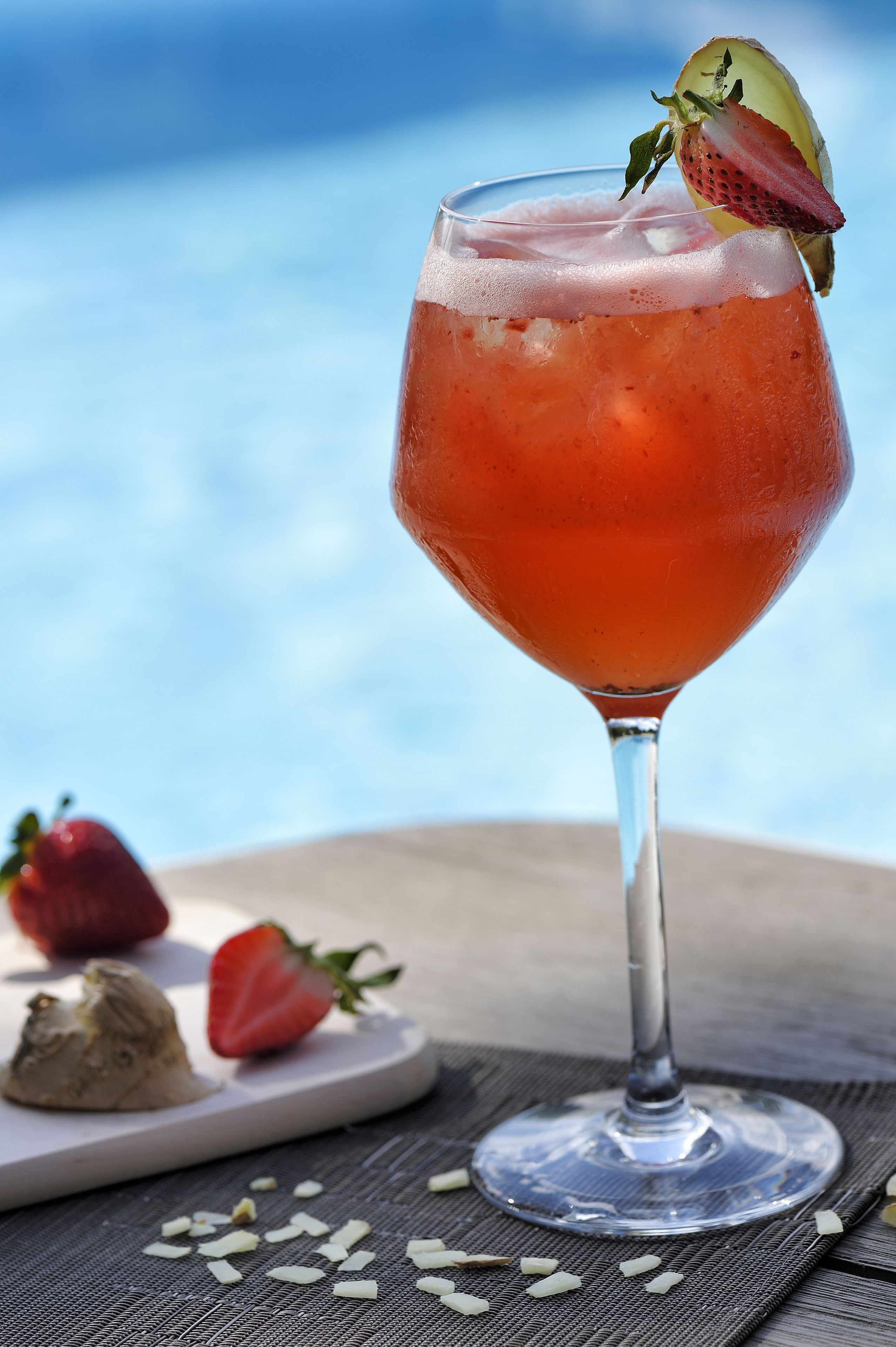 Um copo de cocktail com morango, apoiado sobre uma mesa, com céu visível ao fundo.