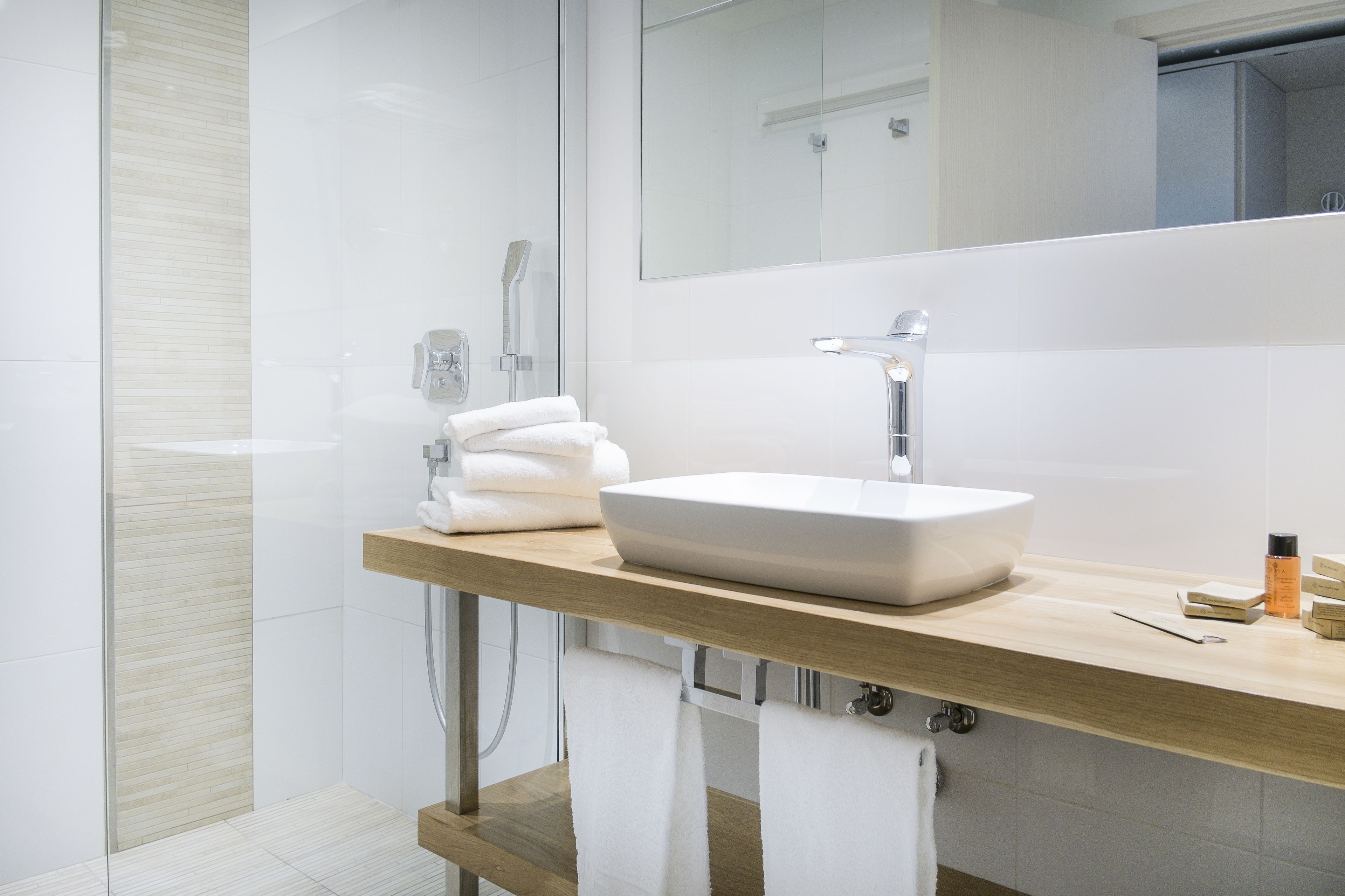 A modern bathroom with a large mirror, a wooden countertop, a white sink, and neatly stacked towels.